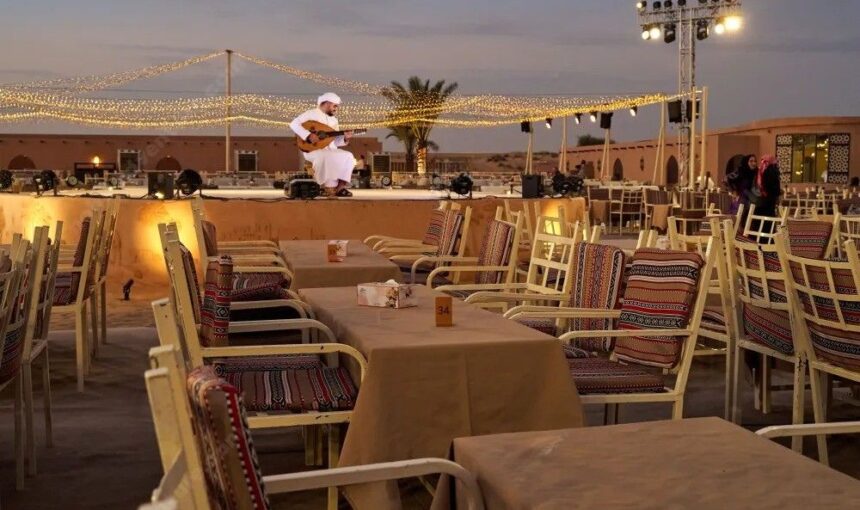 Outdoor dining setup with tables and stage for live performances at Lama Desert Safari Dubai during the evening desert experience.