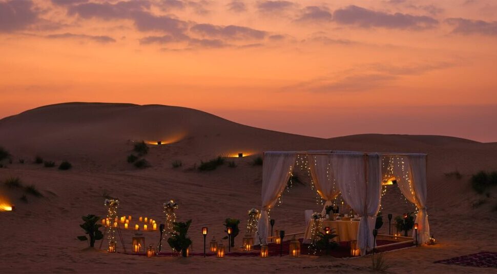 private dinner Dubai desert setup with candles on red dunes at sunset