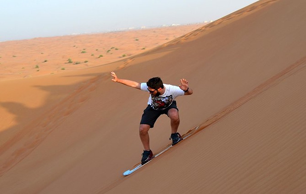 Sandboarding Dubai – Thrilling Desert Adventure on Golden Dunes › Forever Tourism LLC Traveler enjoying sandboarding Dubai adventure down steep golden desert dunes