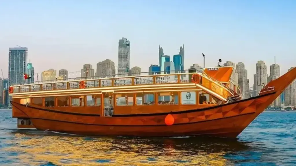 A wooden dhow cruise boat on calm water with a modern city skyline featuring tall towers in the background, highlighting the 2 nights cruise from Dubai experience, along with options like a one night cruise Dubai, a scenic Dubai to Abu Dhabi cruise, and a convenient 1 day cruise from Dubai to Abu Dhabi.
