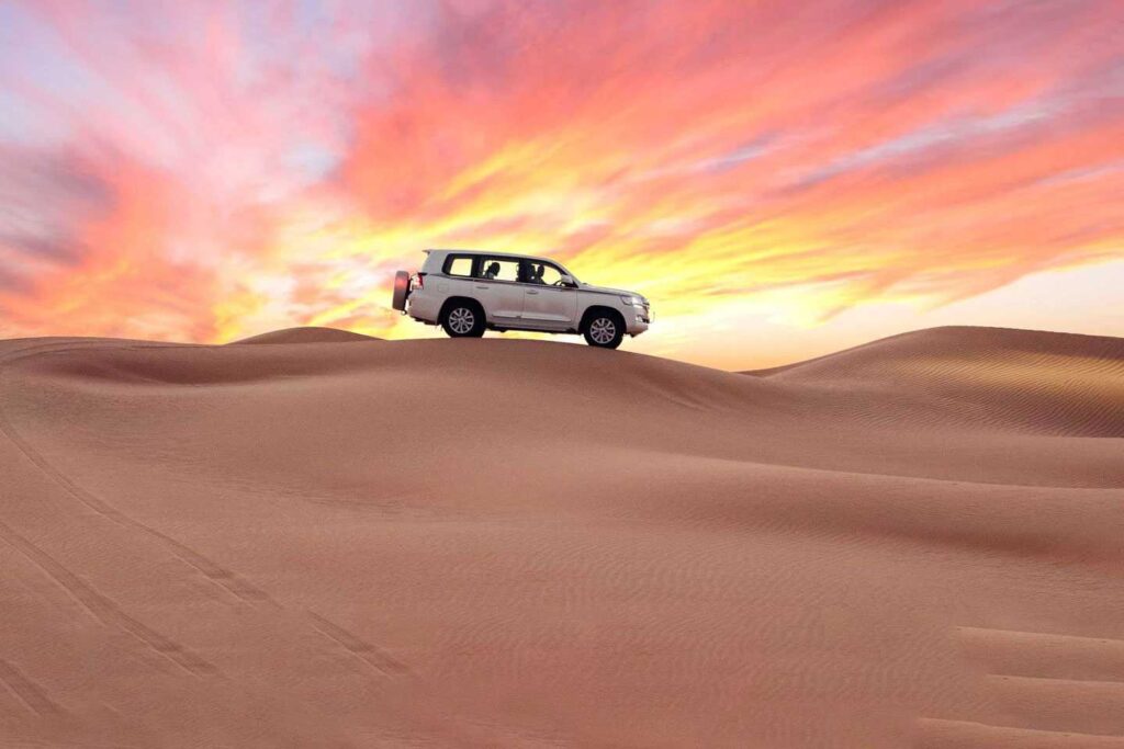 Luxury 4x4 driving over sand dunes during VIP desert safari with BBQ dinner at sunset in Dubai.