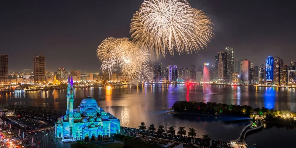 Fireworks in Sharjah lighting up the skyline above the waterfront and iconic mosque during a festive night celebration.