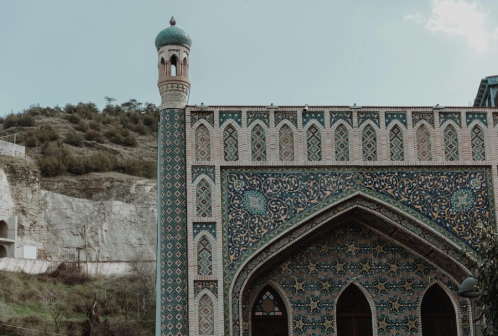 Ornate mosque with intricate tilework and green dome in the Caucasus region, one of the cheapest places to travel from Dubai in Eid