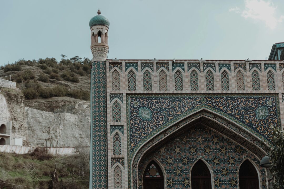 Ornate mosque with intricate tilework and green dome in the Caucasus region, one of the cheapest places to travel from Dubai in Eid