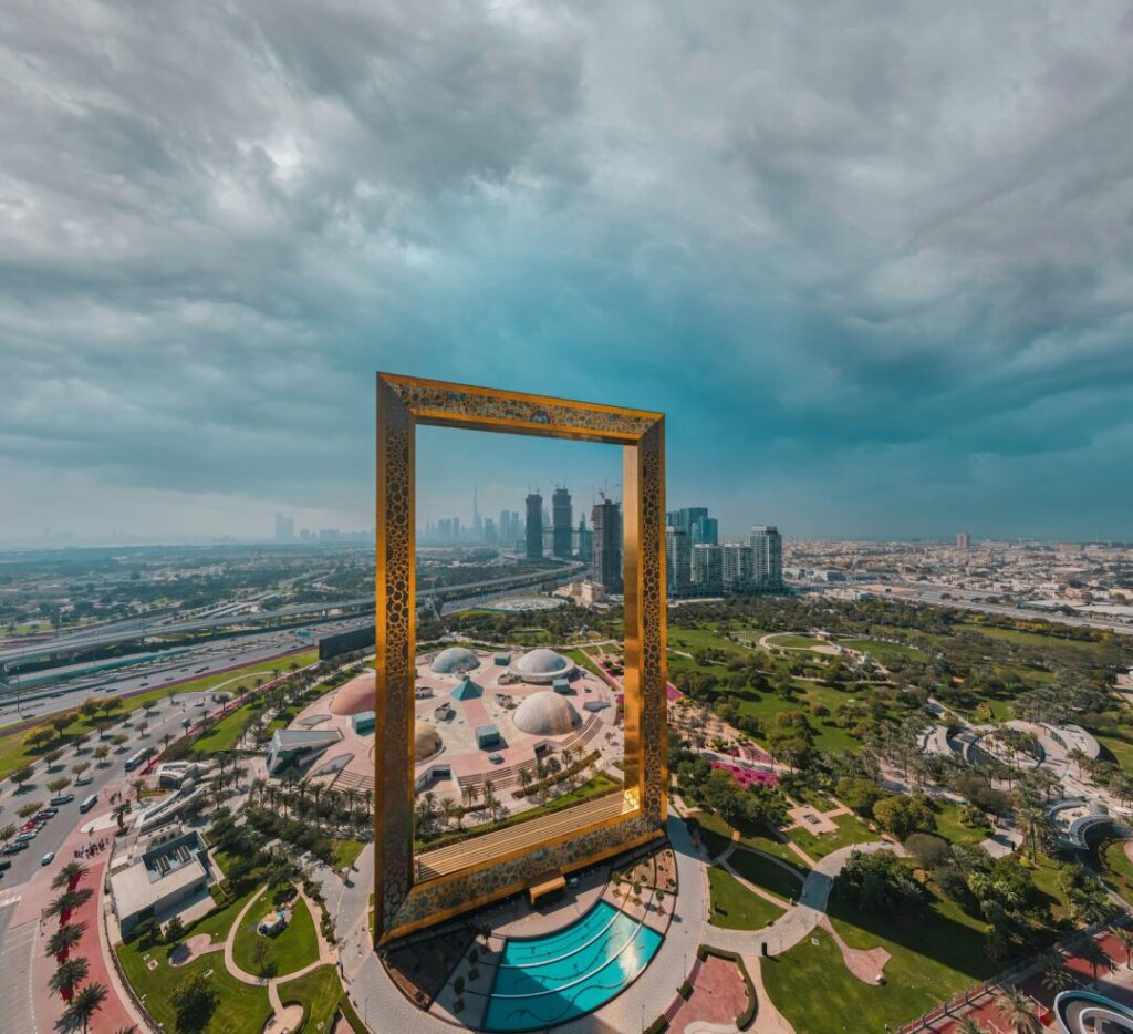 Tall golden rectangular frame sculpture standing over a landscaped park, framing the Dubai skyline beyond.