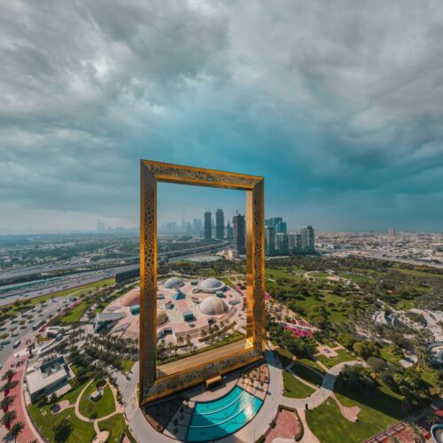 Tall golden rectangular frame sculpture standing over a landscaped park, framing the Dubai skyline beyond.