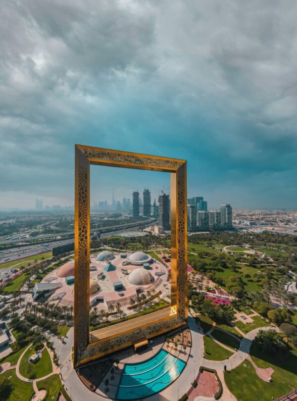 Tall golden rectangular frame sculpture standing over a landscaped park, framing the Dubai skyline beyond.