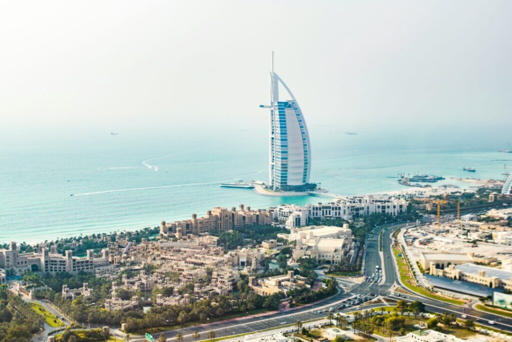 Aerial view of Dubai coast with the sail-shaped Burj Al Arab hotel on the water and surrounding buildings.