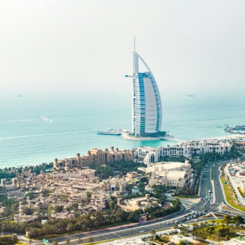 Aerial view of Dubai coast with the sail-shaped Burj Al Arab hotel on the water and surrounding buildings.