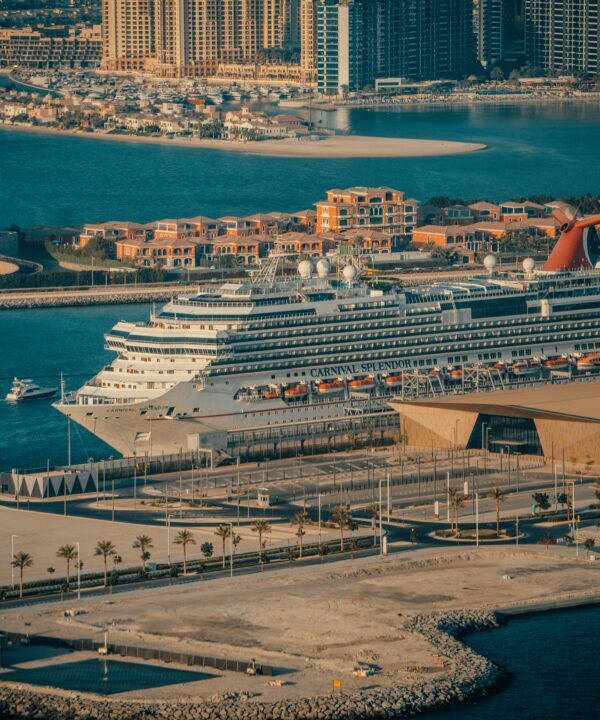 Cruise ship Carnival Splendor docked at a marina with a city skyline and palm-lined promenade in the background.