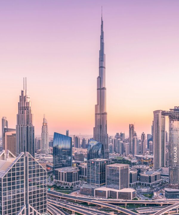 Dubai skyline at sunset with the Burj Khalifa towering above a cluster of skyscrapers and foreground highways.
