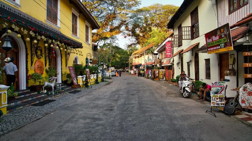 Colorful street in a tourist town with yellow and white buildings, string lights, and pedestrians walking along a quaint shops-lined avenue.