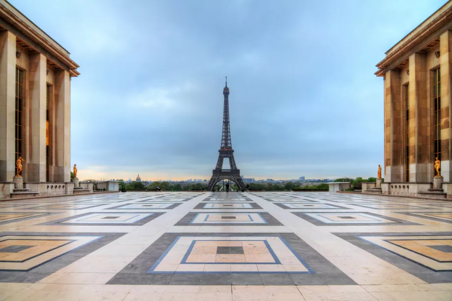 Wide plaza with geometric tile patterns leads the eye to the Eiffel Tower framed by classical buildings on the Trocadéro overlook.