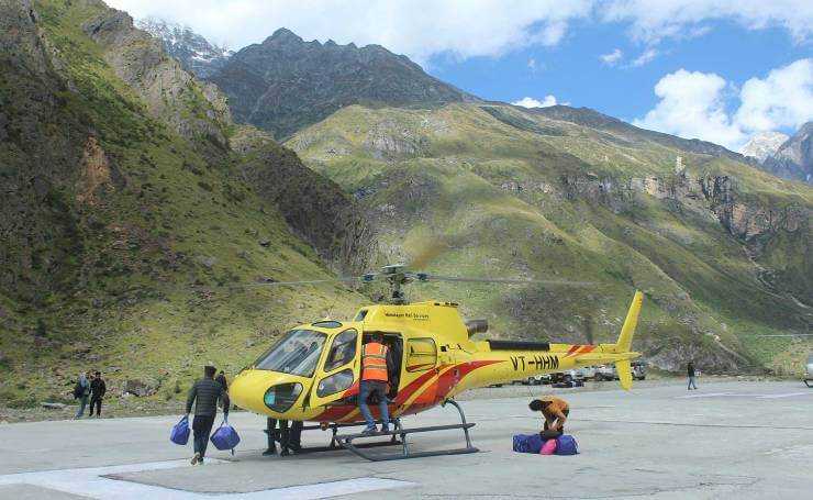 Yellow rescue helicopter on a concrete helipad in a mountainous valley, with people loading gear onto it.