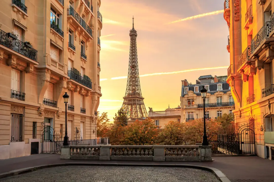 Parisian street at sunset with the Eiffel Tower in the distance, framed by ornate buildings and iron balconies on both sides.