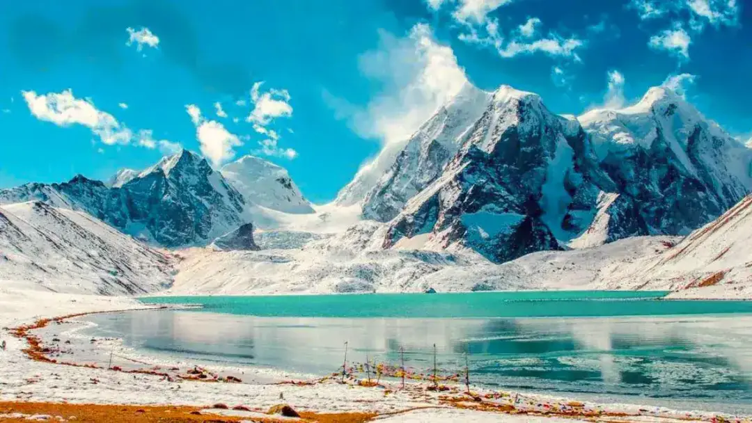Turquoise glacial lake in a snow-covered mountain valley under a bright blue sky with a few clouds.