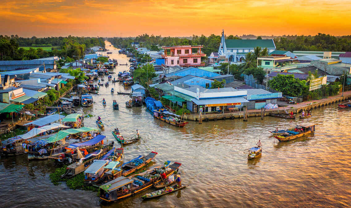 Vibrant riverside market at sunset with numerous boats and colorful buildings along a canal.