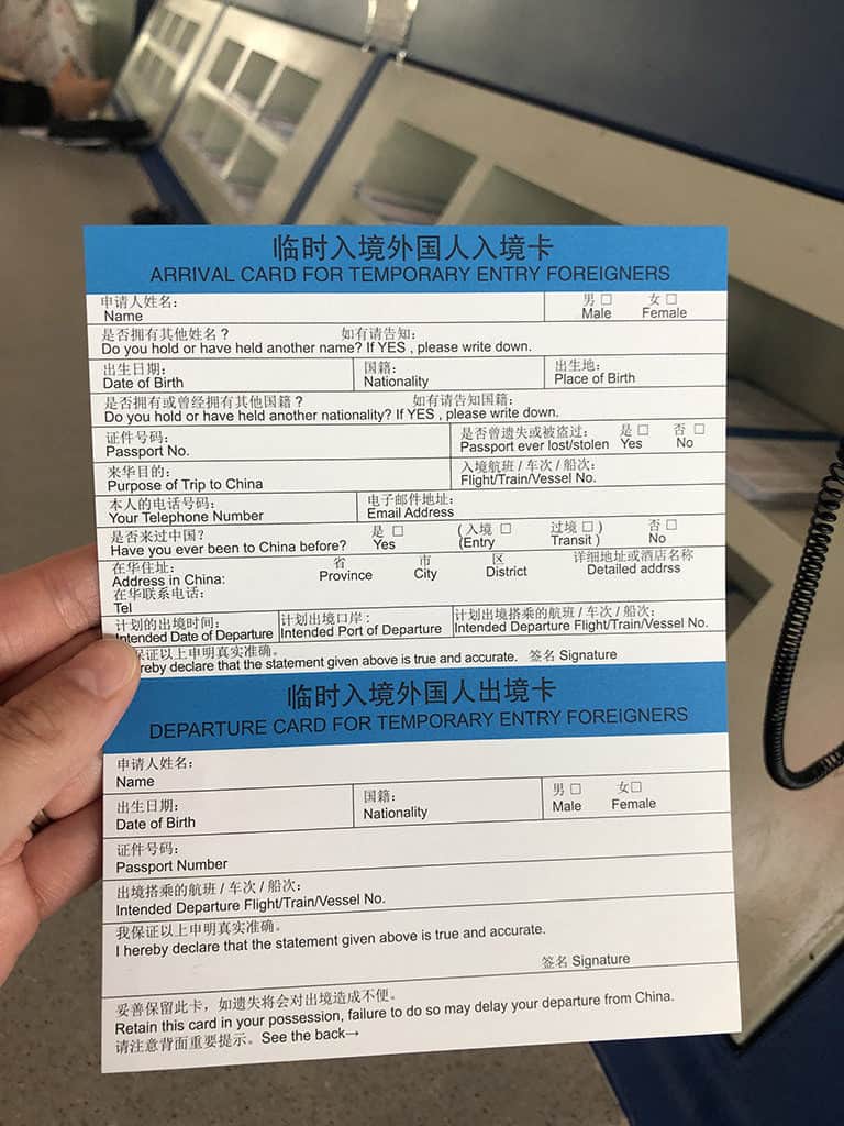 Two bilingual arrival and departure cards for temporary foreign entry, held in a hand, with a blue header and Chinese/English labels at a counter.