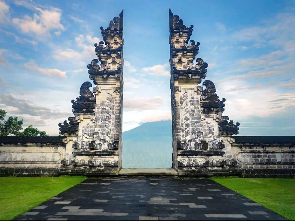 Symmetrical, ornate stone split gateway with dragon carvings opens to a distant mountain and blue sky.