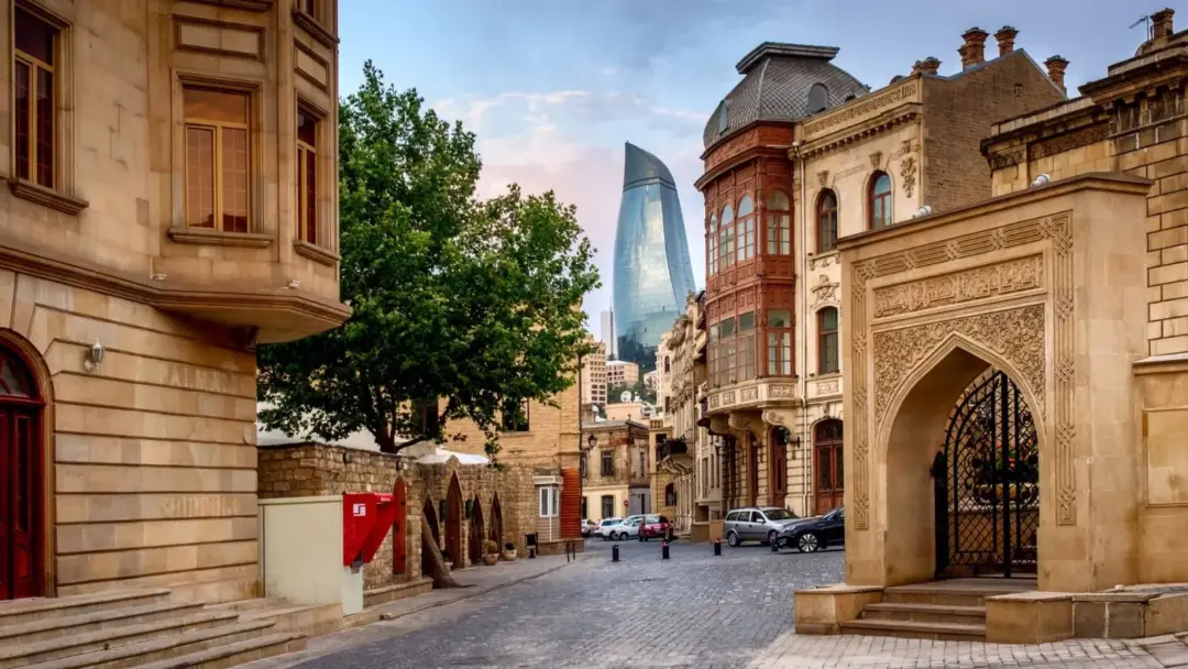 Historic street in a European-style district with ornate archway, cobblestone road, and a modern glass skyscraper in the distance.