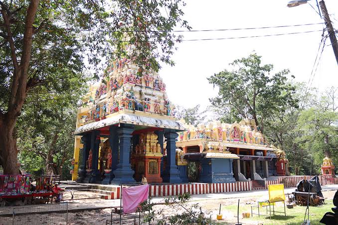 Colorful Hindu temple with ornate tiered tower and blue pillars in a shaded outdoor area. (Informative image)